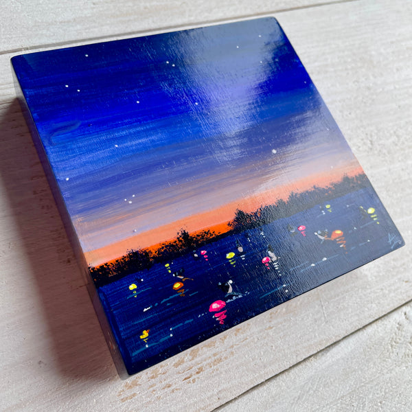 Small painting of a night scene with swimmers and colorful tow floats over water on a textured surface.