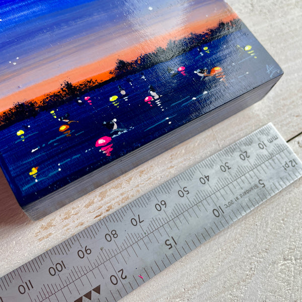 Painting of a night scene with people swimming and glowing tow floats, next to a ruler for scale.