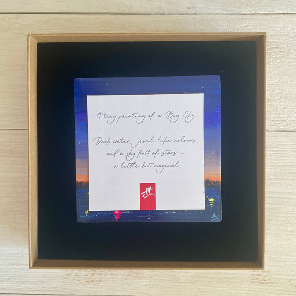 Boxed artwork with description card on a wooden surface
