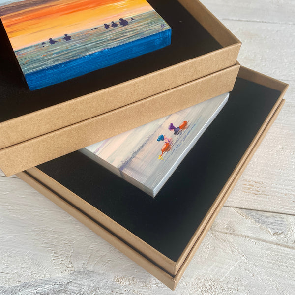 Two boxed miniature paintings stacked on a wooden background