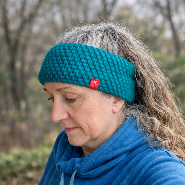 Person wearing a narrow band teal knitted headband with a red Andrea Hall label outdoors