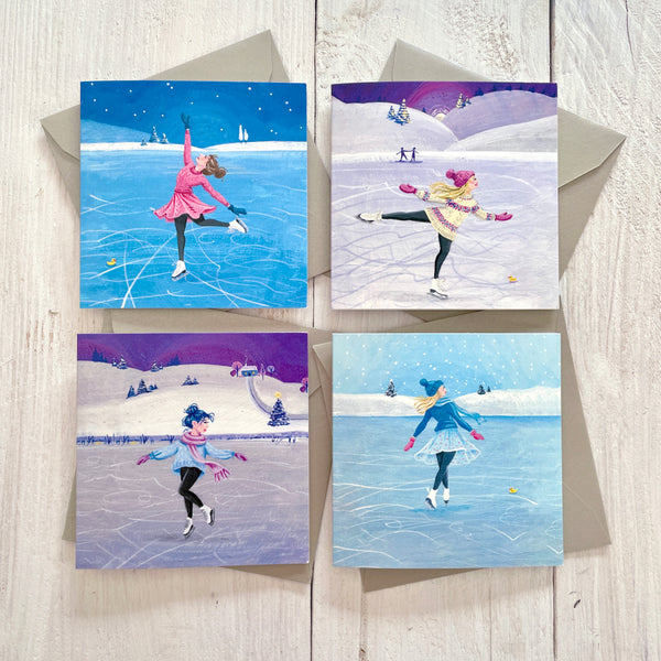 Set of four mini greetings cards featuring ice skaters on frozen lakes, with silver pearlescent envelopes