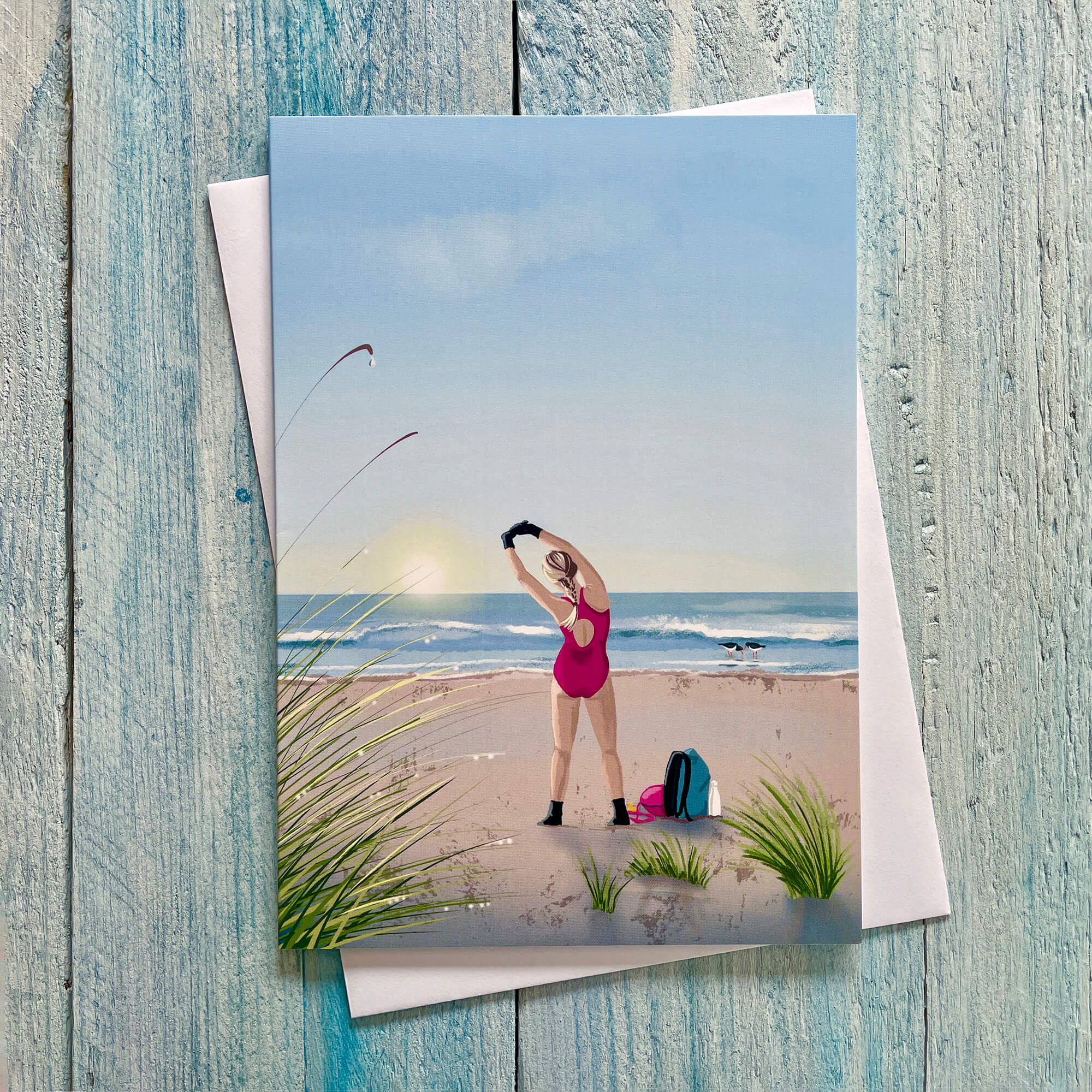 Greetings card illustration of a wild swimmer stretching on the beach at sunrise.