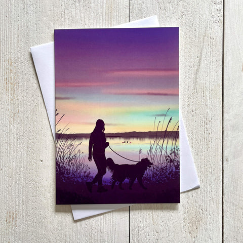 Greeting card with a silhouette of a person walking a dog at sunset, with a white envelope