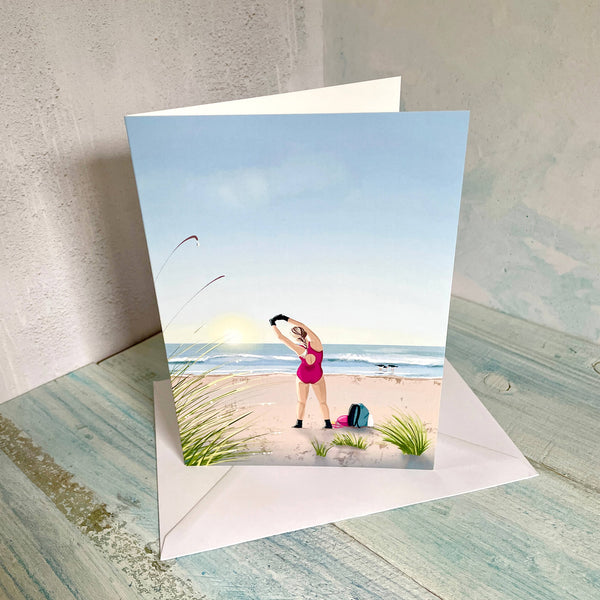 Greetings card illustration of a wild swimmer stretching on the beach at sunrise.