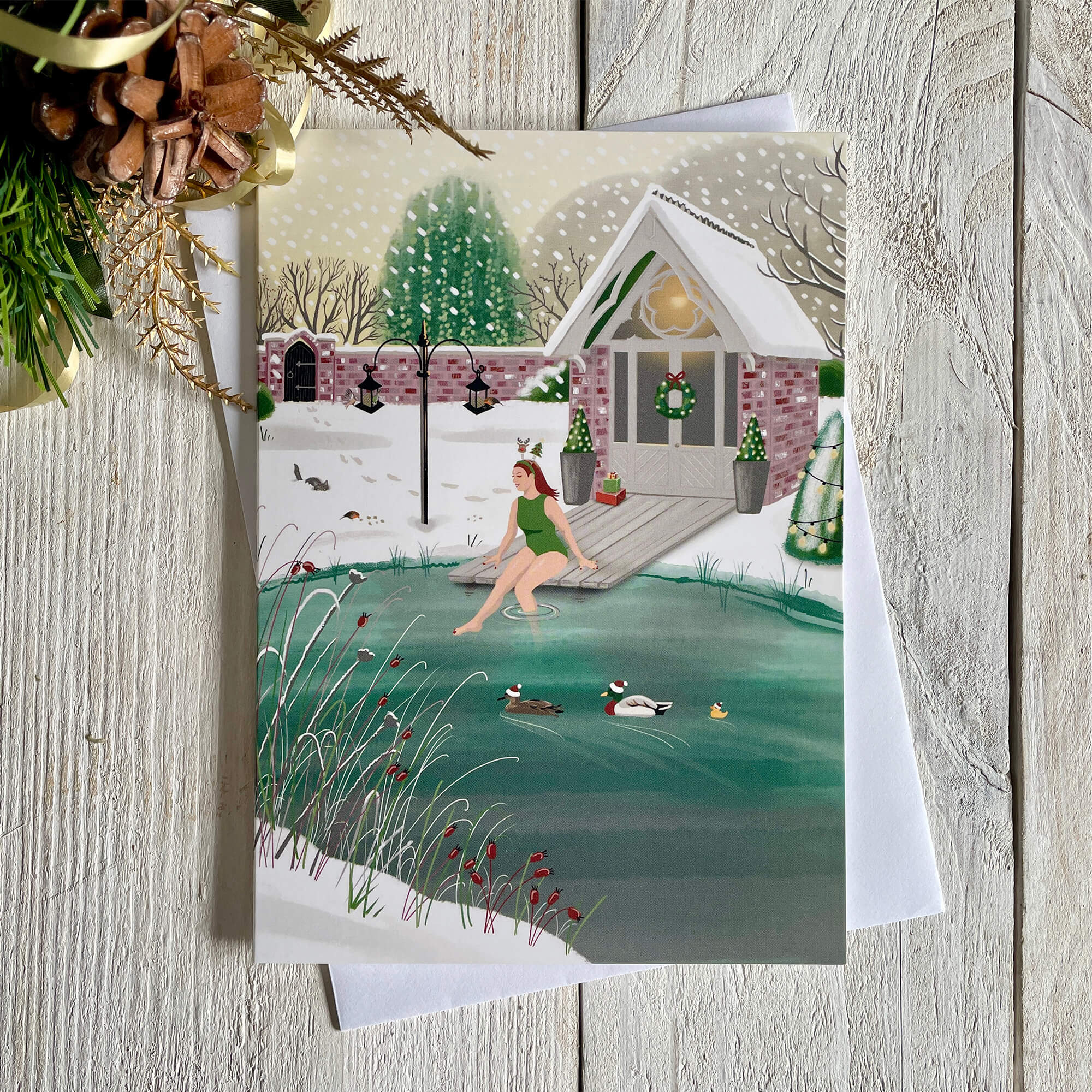 Christmas card with illustration of wild swimmer getting into her garden pond. Card with white envelope and a touch of Christmas decoration