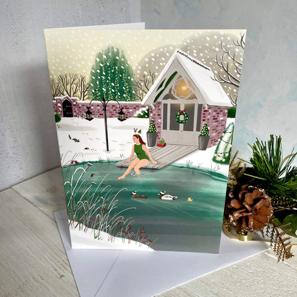 Christmas card with illustration of wild swimmer getting into her garden pond. Standing card with Christmas decoration