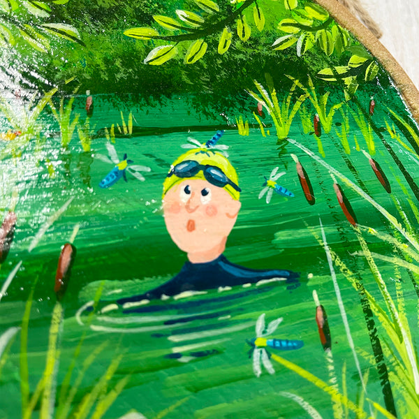 Close-up of wild swimming scene painted on round natural log slice with bark edge.