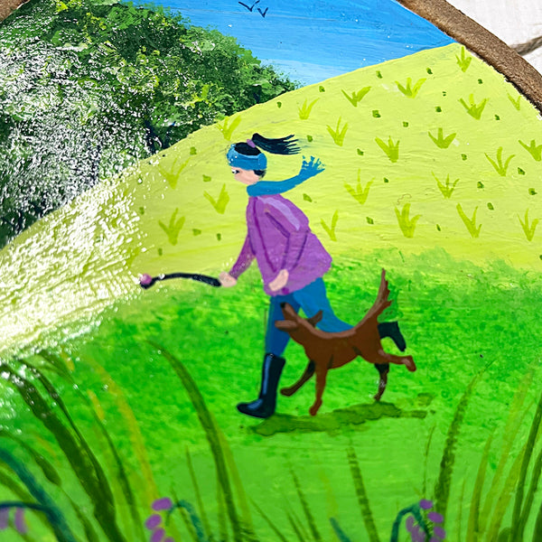 Close-up of countryside dog walk illustration painted on natural log slice with bark edge.