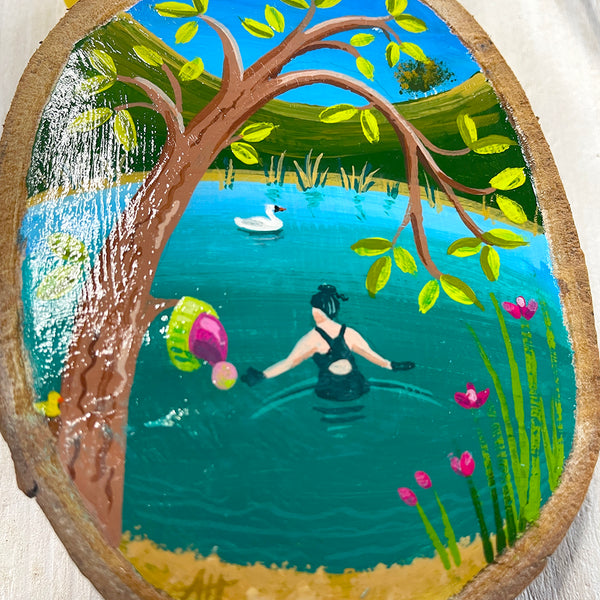 Close-up of tiny pond swim scene painted on natural oval log slice with bark edge.
