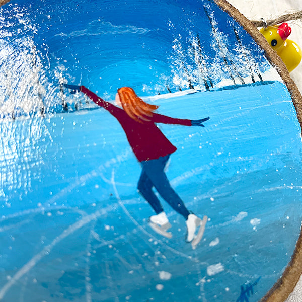Close-up of ice skating scene painted on round natural log slice with bark edge.