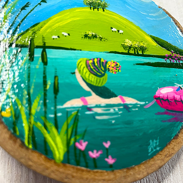 Close-up of wild swimming scene painted on natural log slice with bark edge.