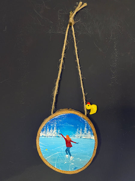 Original painted log slice decoration featuring a winter skating scene hanging against a blackboard background.