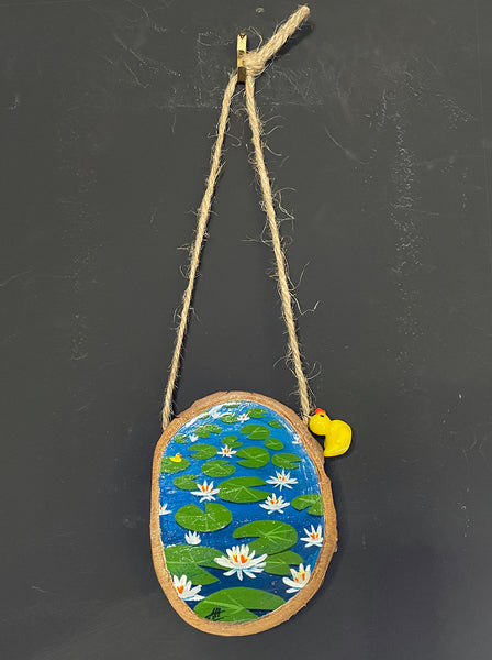 Original painted log slice decoration featuring a lily pond scene hanging against a blackboard background.