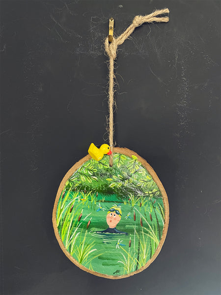 Original hand-painted log slice decoration hanging with a little yellow Ducky charm against a blackboard background.