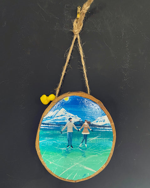 Original painted log slice decoration featuring a winter ice skating scene hanging against a blackboard background