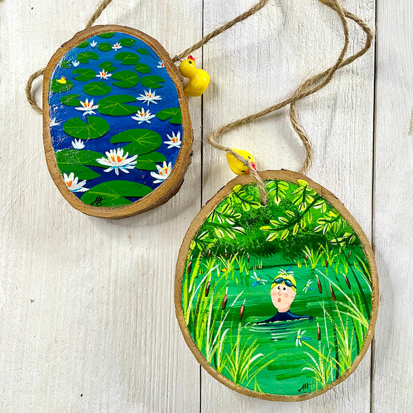 Two log-slice decorations with hand painted wild swimming illustrations and Ducky charms
