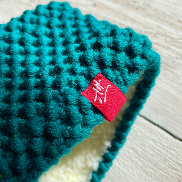 Detail of teal knitted headband with a red Andrea Hall logo hem tag