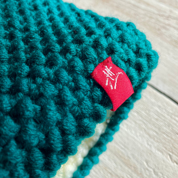 Detail of a teal knitted headband with a red Andrea Hall tag