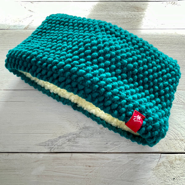 Teal hand-knitted headband with a red Andrea Hall tag