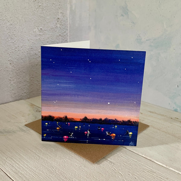 Mini greeting card of swimmers with colourful tow floats under a starry night sky standing on a wooden surface.