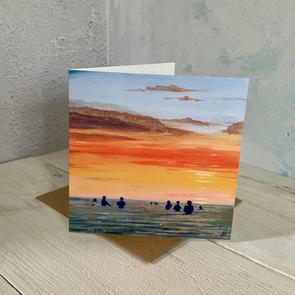 Greeting card with sea swimmers at sunset standing on a wooden surface.