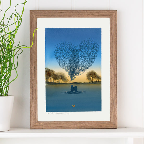Illustration of two swimmers in a lake at sunset watching a heart-shaped murmuration of starlings, presented in an oak frame