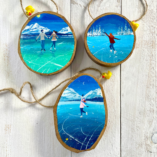 A set of 3 painted log slices depicting natural ice skating scenes with snowy mountains and trees