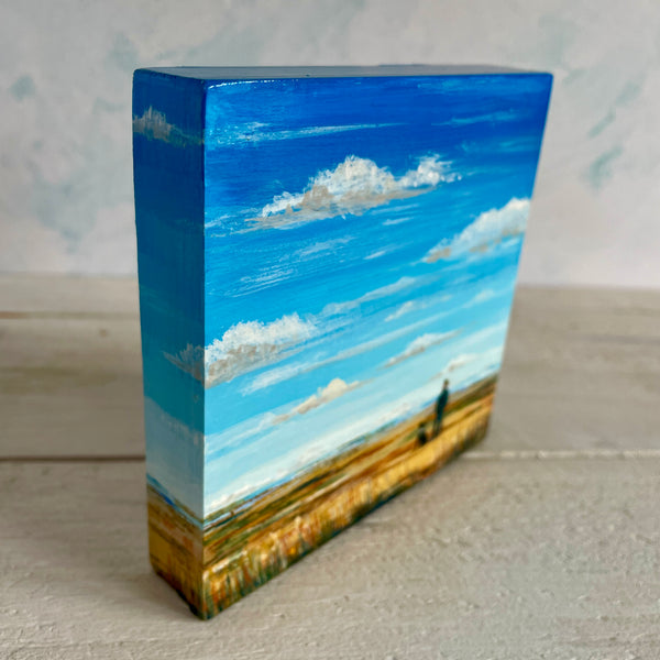 Rectangular block with a painted landscape of a big blue sky and field.