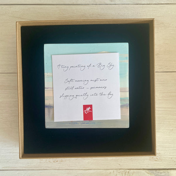 Boxed artwork with description card on a wooden surface