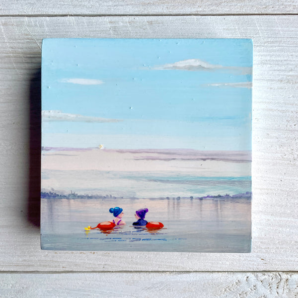 Two swimmers with colorful tow floats on a calm misty lake.