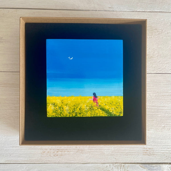 Original miniature Big Sky painting of rapeseed fields beneath a blue sky with a figure walking through. Presented in display box
