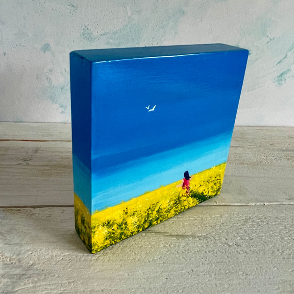 Original Big Sky painting of rapeseed fields beneath a blue sky with a figure walking through. Shown standing