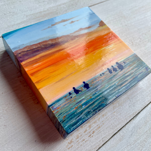 Original miniature painting of a sunset over water with silhouettes of swimmers on a wooden panel.