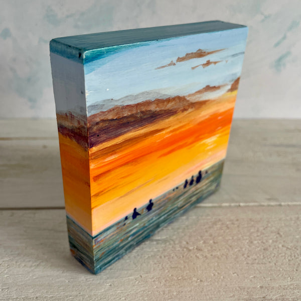 Rectangular wooden block with a painted landscape design on a neutral background