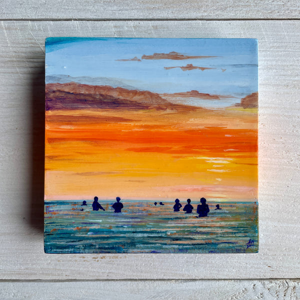 Miniature painting of a sunset over water with silhouettes of swimmers, on a wooden panel.