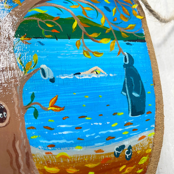 lose-up of hand-painted autumn swim illustration on natural wood slice with bark edge.