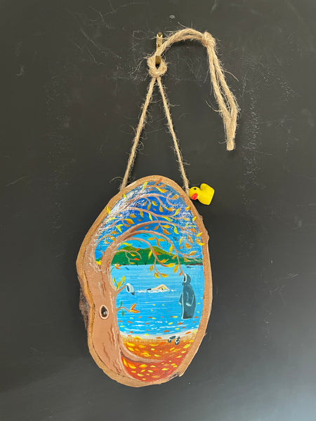 Original painted wood slice decoration hanging on twine with a small Ducky charm against a blackboard background.