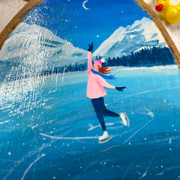 Close-up of ice skating scene painted on natural wood slice with bark edge.