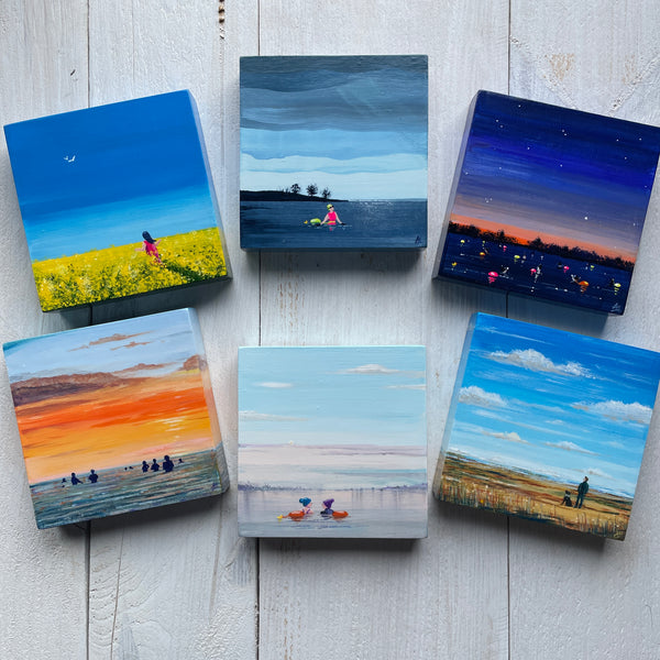 Set of six small square paintings depicting various landscapes on a wooden surface.