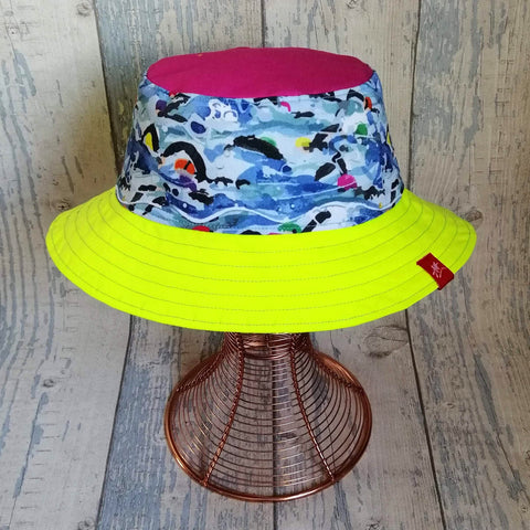 Reversible neon bucket hat with Andrea's iconic Mass Start swimmers design yellow and pink